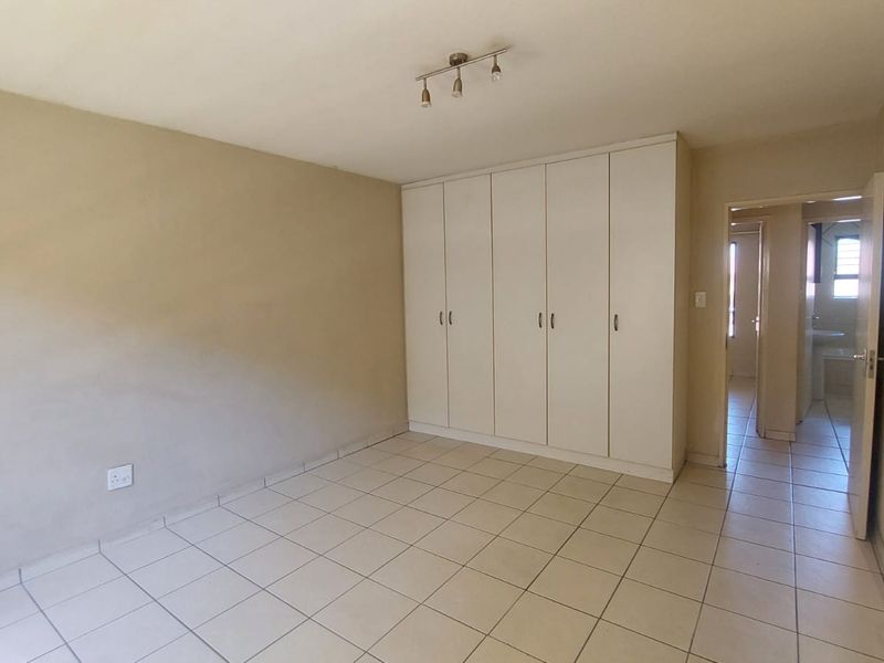 A spacious, empty bedroom featuring neutral tiled flooring, built-in white cupboards, and a modern ceiling-mounted spotlight fixture.