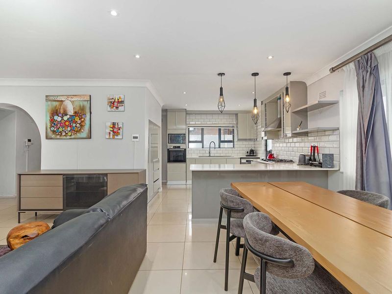 Modern open-plan living and kitchen area featuring sleek cabinetry, stone countertops, subway tile backsplash, and high-quality porcelain floor tiles throughout.
