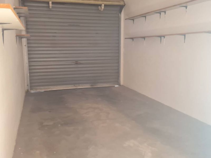 A functional single garage space featuring a secure roller shutter door and practical wall-mounted shelving units for storage.