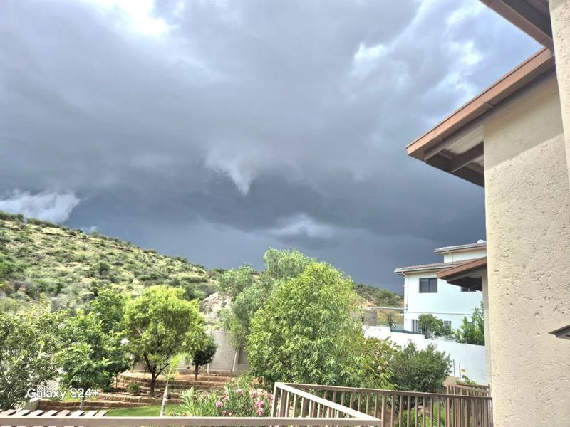 A view from a balcony overlooking a garden and hillside under a stormy sky.