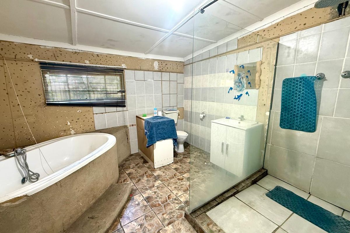 A bathroom featuring a freestanding tub, glass shower enclosure, and vanity, currently requiring significant cosmetic renovation and wall finishing.