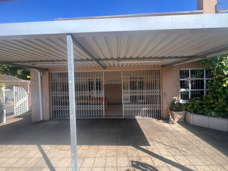 A covered outdoor patio area featuring tiled flooring, a metal carport structure, and secure metal gates providing access to the home.