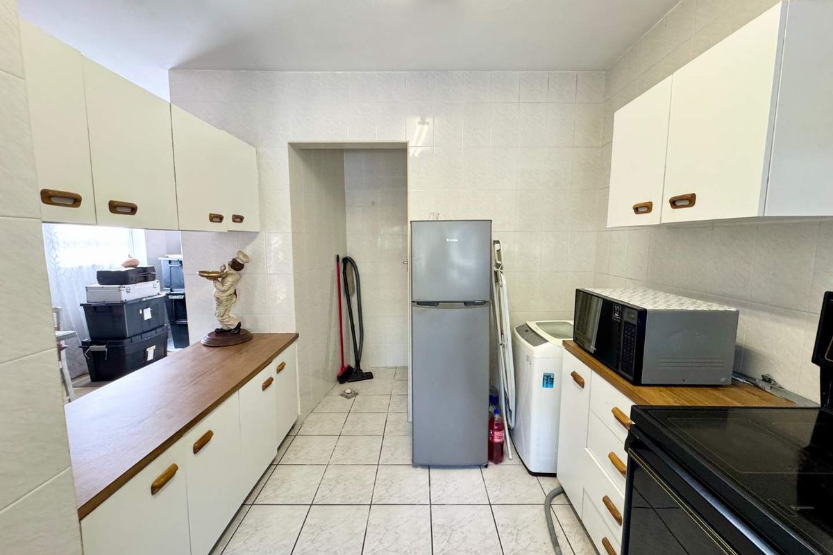 A functional kitchen featuring white cabinetry, laminate countertops, and tiled finishes throughout, providing a practical workspace with integrated stove and storage.