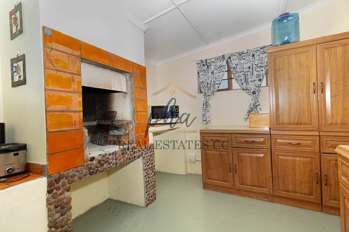 Indoor entertainment area featuring a built-in brick braai fireplace and wooden cabinetry for storage.