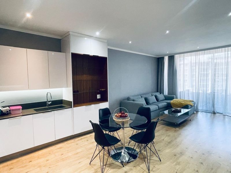Modern open-plan living area featuring a sleek kitchen with built-in cabinetry, recessed lighting, and light wood-look flooring, seamlessly flowing into the lounge space.