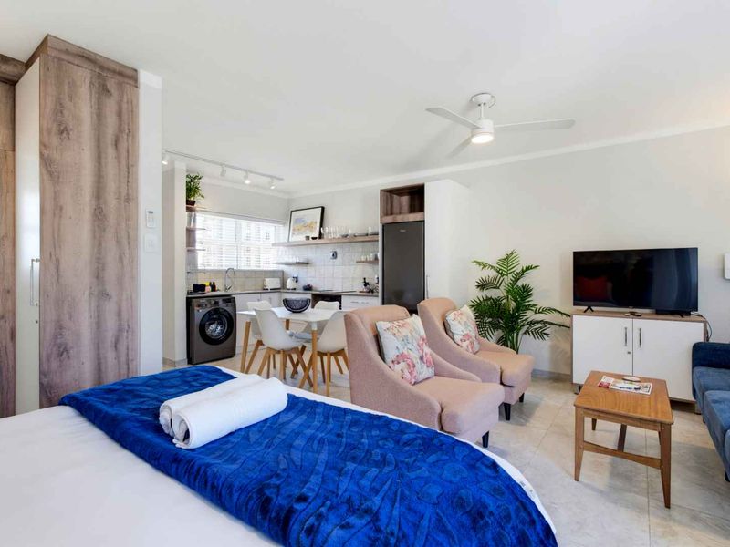 An open-plan studio apartment featuring a compact kitchen area, tiled flooring, and a ceiling fan, creating a functional and well-maintained living space.