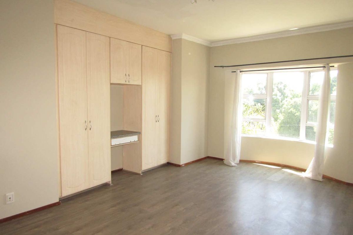 Spacious bedroom featuring light wood built-in cupboards with an integrated desk area and large windows providing natural light.