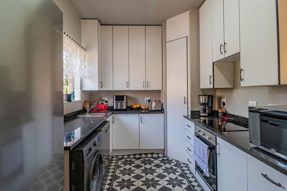 A functional kitchen featuring white cabinetry, dark granite countertops, a built-in oven, electric hob, and decorative patterned floor tiles.