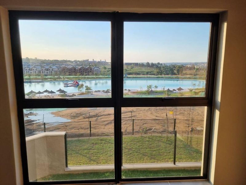 A clear view through a modern aluminium window overlooking a landscaped estate with a central water feature and recreational area.