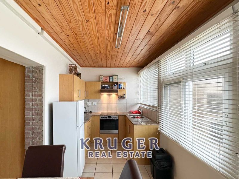 A functional kitchen featuring timber ceiling paneling, laminate cabinetry, built-in oven with extractor fan, and large windows with venetian blinds.