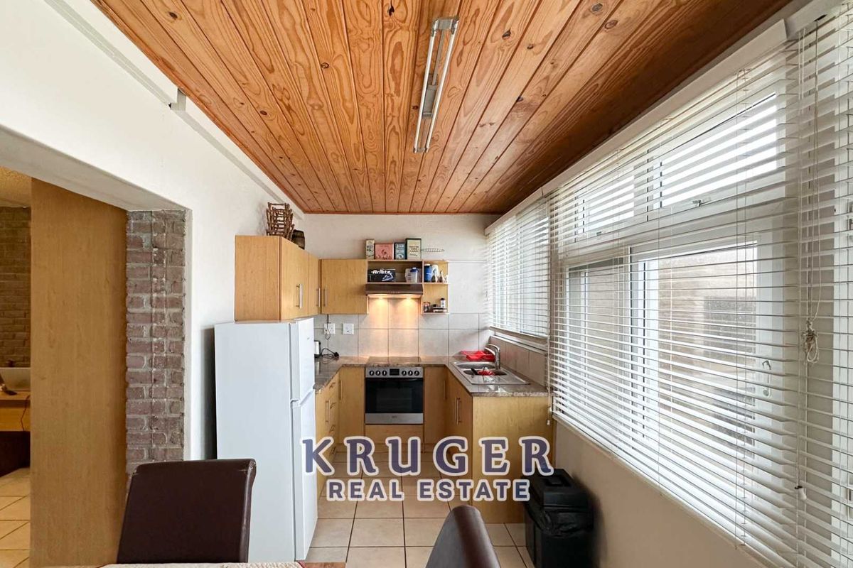 A functional kitchen featuring timber ceiling paneling, laminate cabinetry, built-in oven with extractor fan, and large windows with venetian blinds.