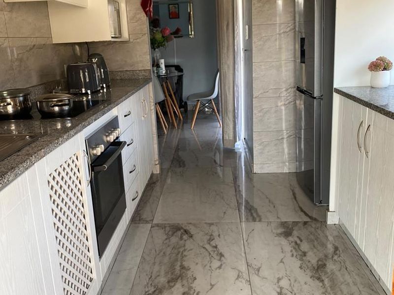 A functional kitchen featuring white cabinetry, granite countertops, built-in oven, extractor fan, and modern marble-look floor tiles.