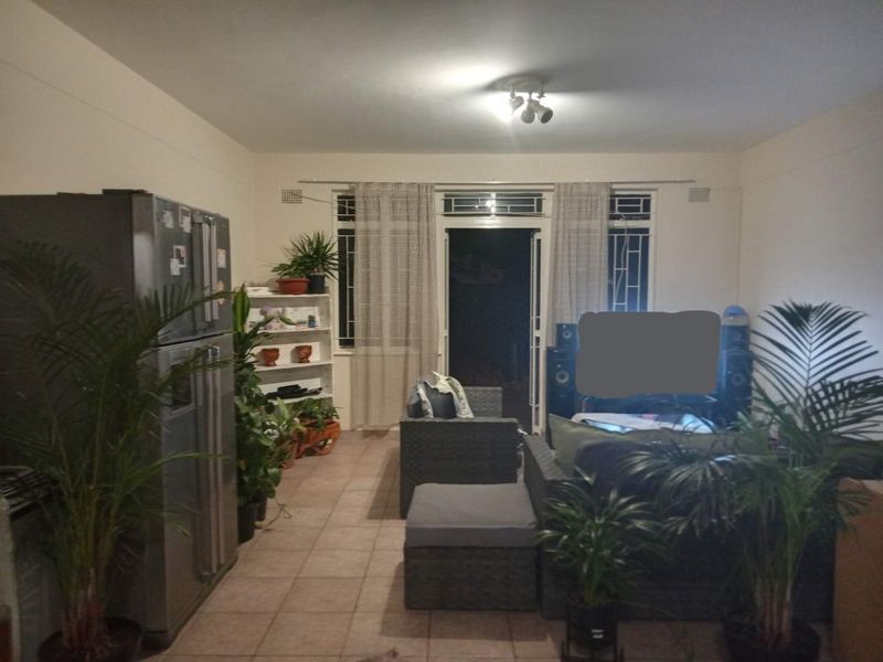 A living room area featuring tiled flooring and a sliding glass door with security gate leading to an outdoor space.