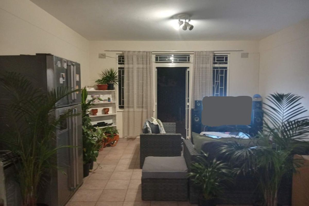 A living room area featuring tiled flooring and a sliding glass door with security gate leading to an outdoor space.