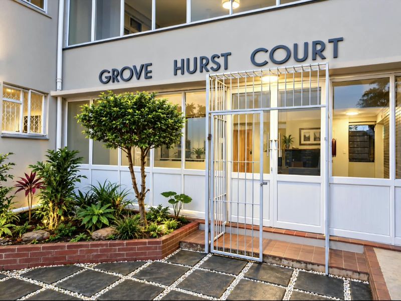 The front entrance of Grove Hurst Court featuring a secure gated access, a well-maintained brick planter box, and paved courtyard area.