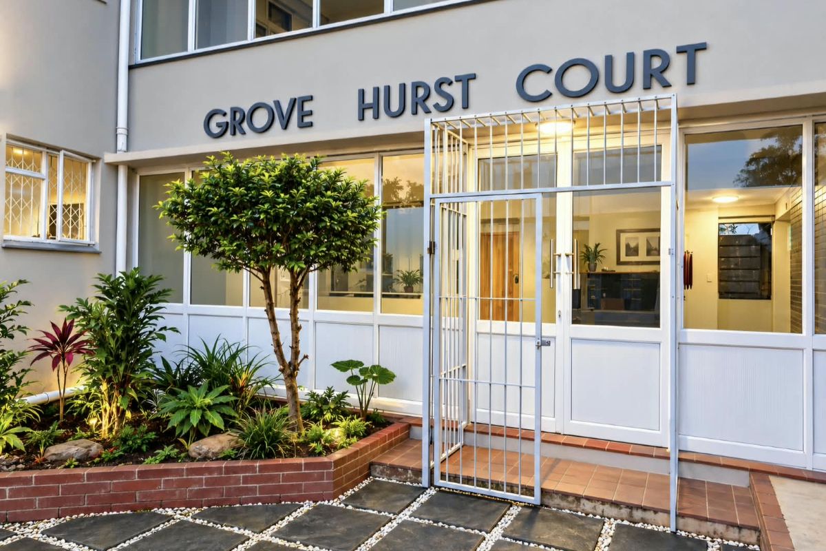 The front entrance of Grove Hurst Court featuring a secure gated access, a well-maintained brick planter box, and paved courtyard area.
