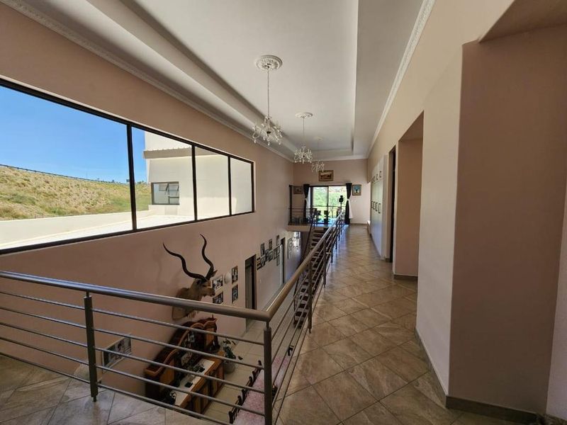 Spacious upper-level hallway featuring tiled flooring, a modern stainless steel balustrade, and large windows providing ample natural light and scenic views.