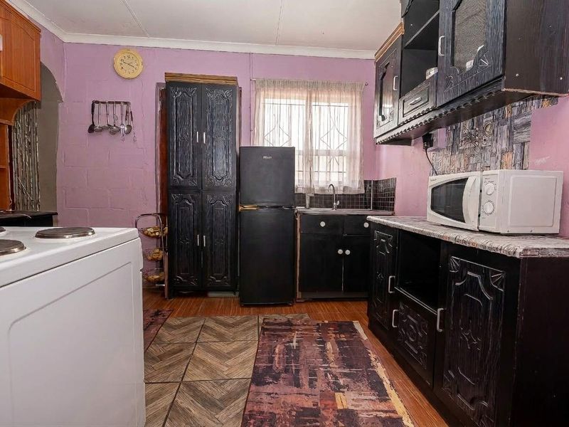 A functional kitchen featuring dark built-in cabinetry, a tiled backsplash, and laminate flooring, offering potential for a modern cosmetic update.