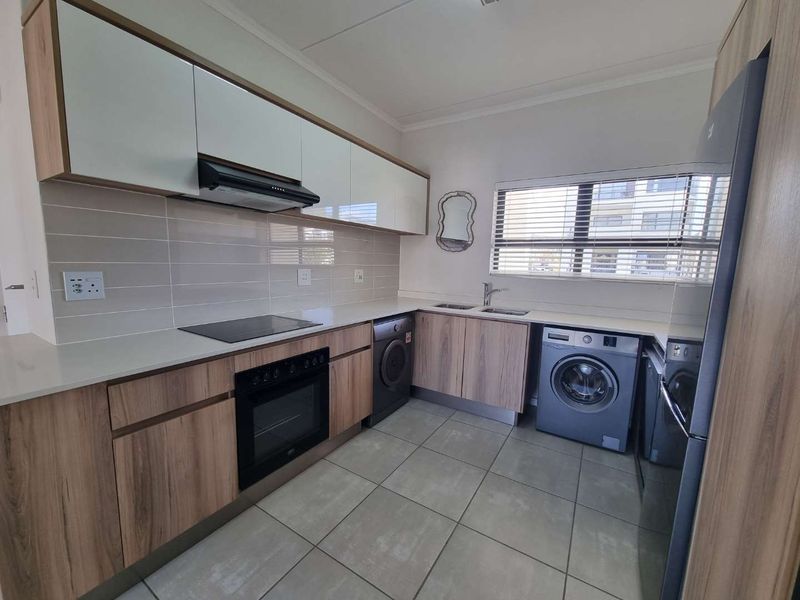 Modern kitchen featuring wood-grain cabinetry, stone countertops, integrated electric hob and oven, tiled backsplash, and dedicated space for laundry appliances.