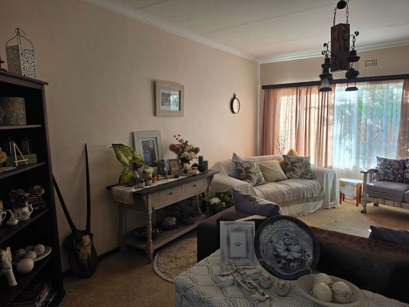 A cozy living room featuring carpeted flooring, cove cornicing, and a large window with natural light, providing a comfortable and inviting living space.