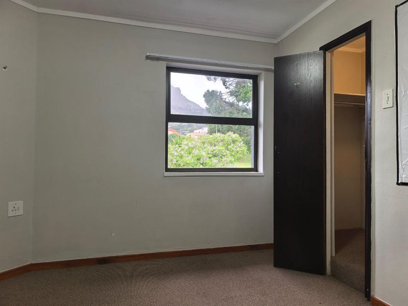 An empty bedroom featuring carpeted flooring, a built-in cupboard, and a window with views of the surrounding landscape.