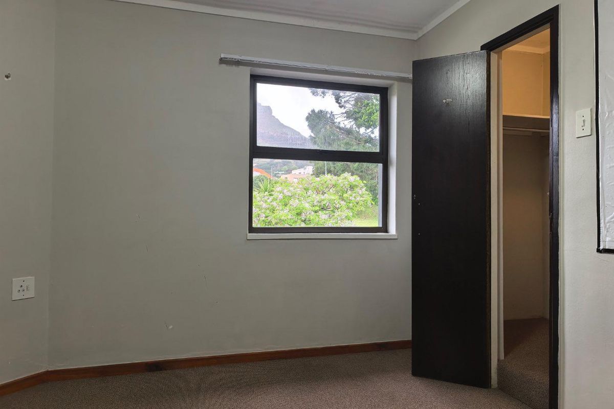 An empty bedroom featuring carpeted flooring, a built-in cupboard, and a window with views of the surrounding landscape.