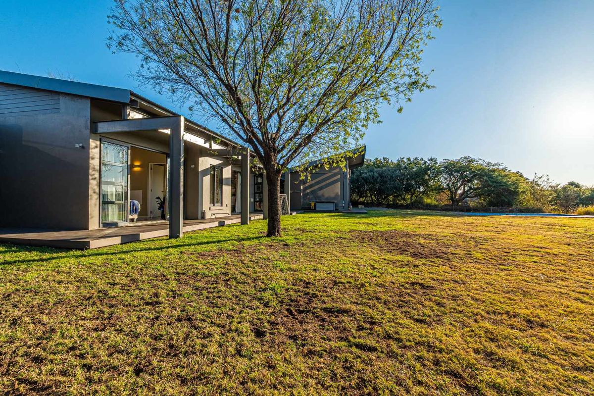 A view of the rear exterior of the house featuring a covered patio, modern architectural lines, and a spacious lawn area.