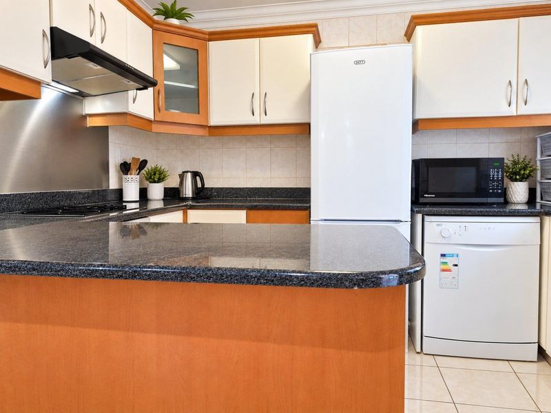 A functional kitchen featuring laminate cabinetry, granite countertops, tiled backsplash, and integrated appliances, offering a practical layout for daily use.