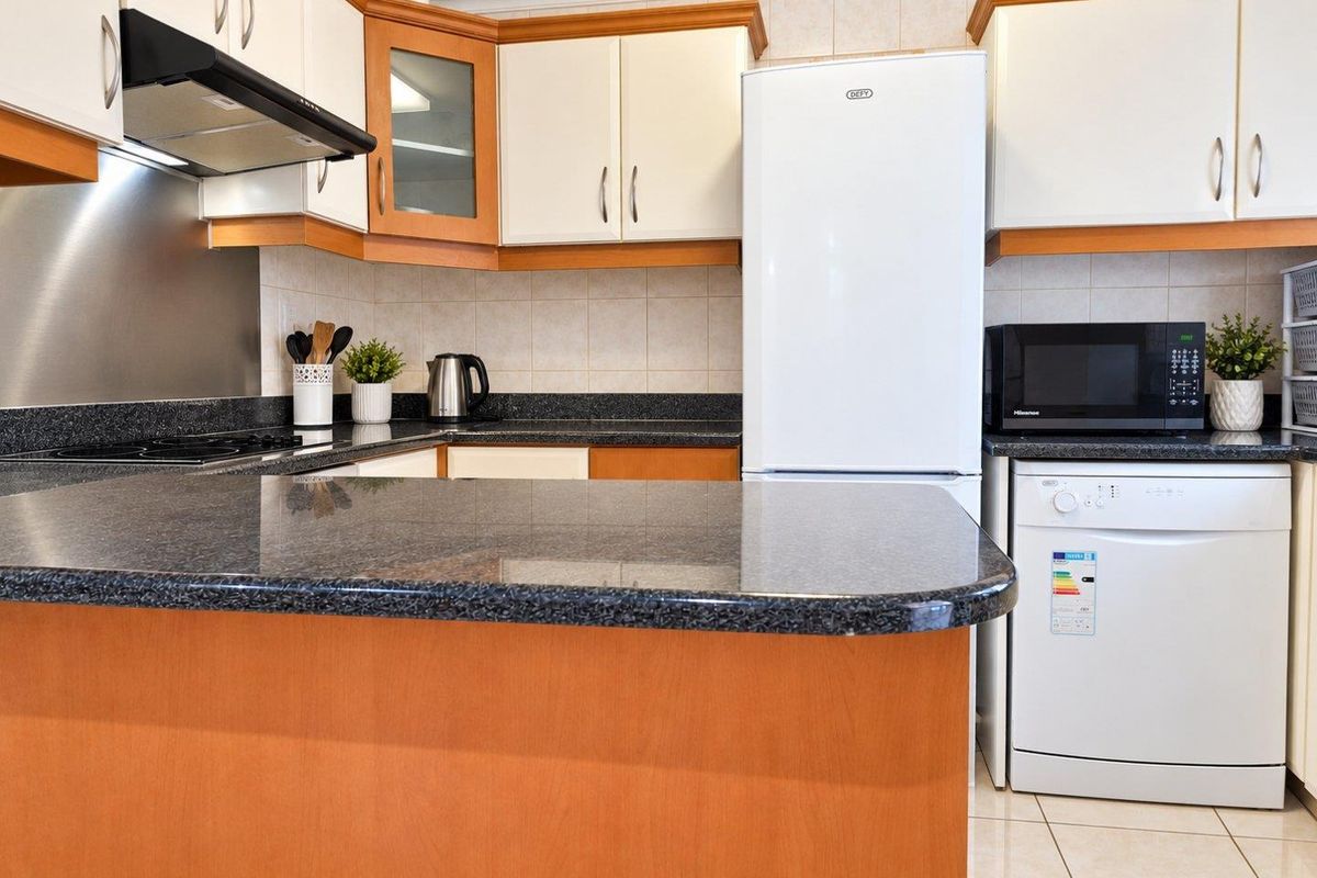 A functional kitchen featuring laminate cabinetry, granite countertops, tiled backsplash, and integrated appliances, offering a practical layout for daily use.