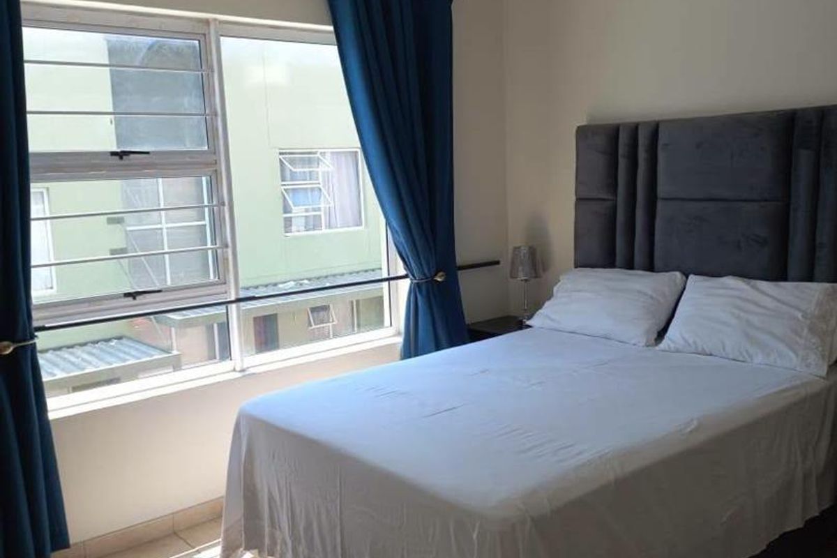 A functional bedroom featuring tiled flooring, aluminium window frames with security bars, and neutral wall finishes.