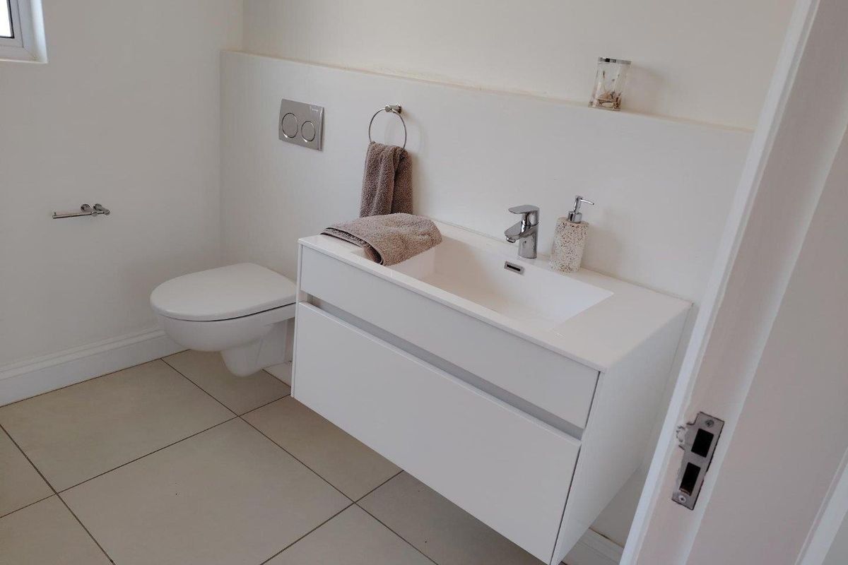 A modern, minimalist bathroom featuring a wall-hung toilet with a concealed cistern and a sleek white vanity cabinet with an integrated basin.