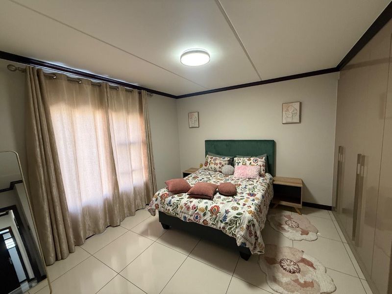 A well-maintained bedroom featuring neutral tiled flooring, built-in cupboards, and large windows with curtains, providing a bright and functional living space.