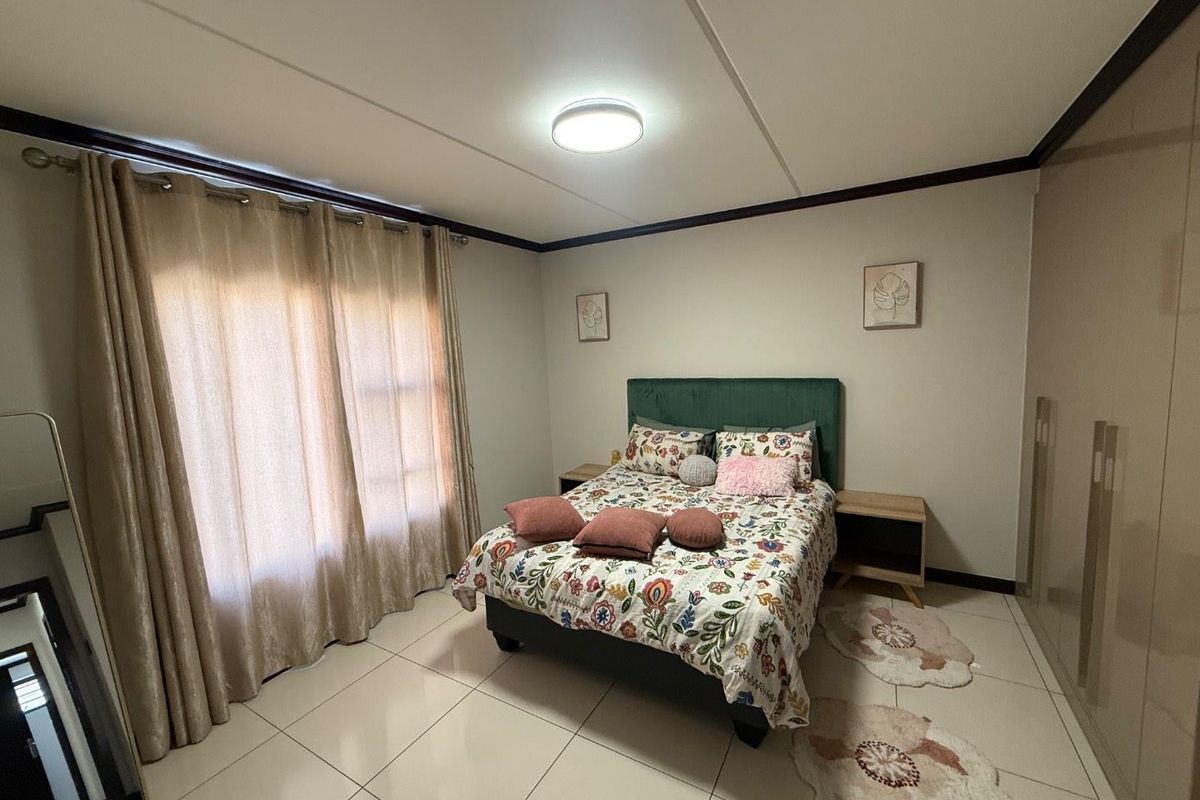 A well-maintained bedroom featuring neutral tiled flooring, built-in cupboards, and large windows with curtains, providing a bright and functional living space.
