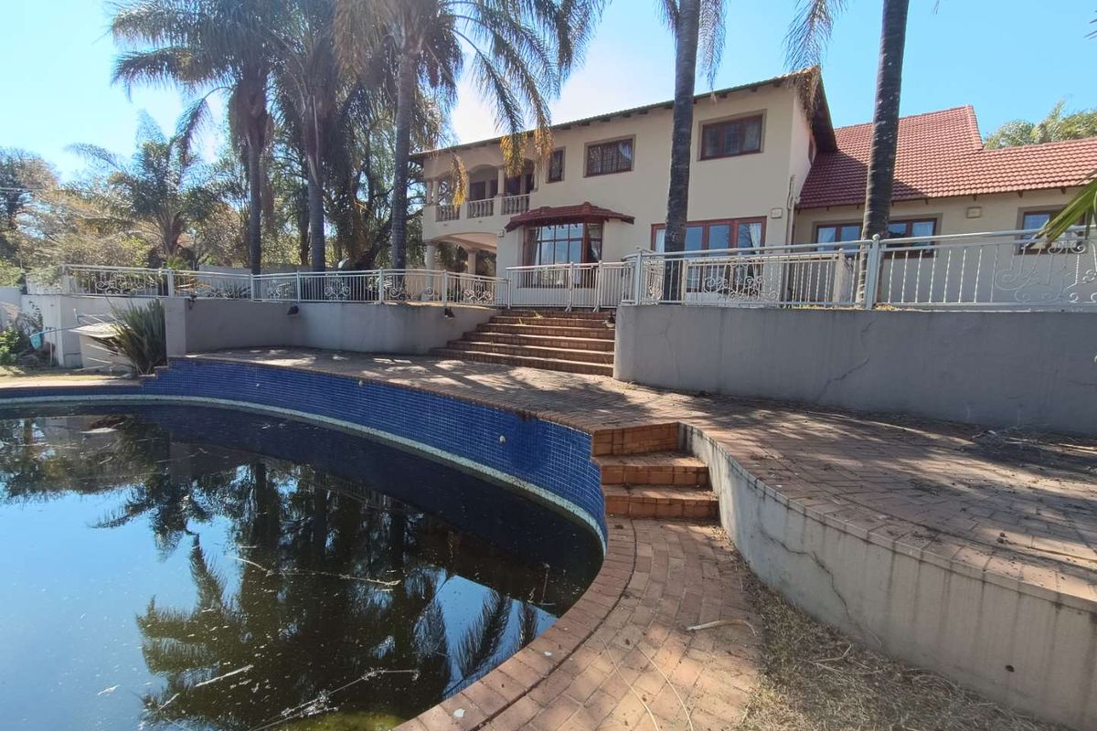 Rear exterior view of the house featuring a large swimming pool, brick paved terrace, and elevated patio area with metal balustrades.