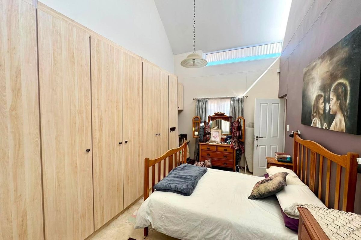 Spacious bedroom featuring extensive built-in cupboards, a high vaulted ceiling with a clerestory window, and neutral finishes.