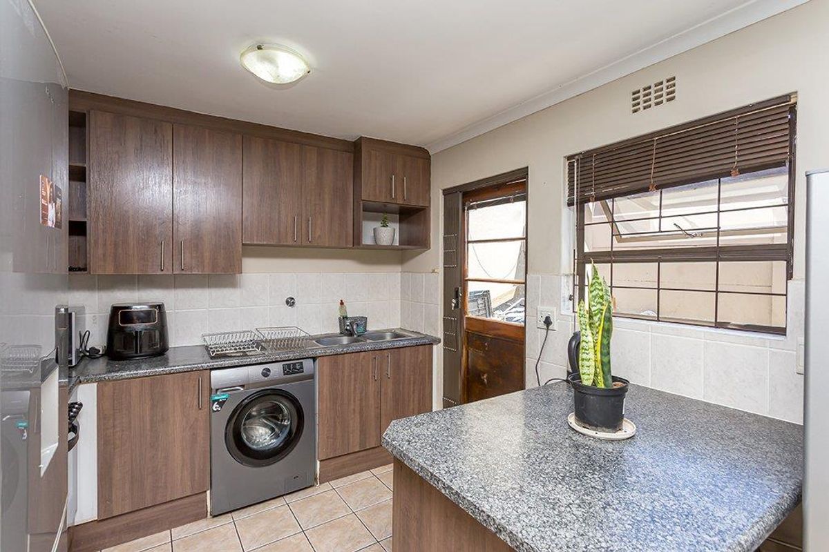 Functional kitchen featuring wood-look laminate cabinetry, granite countertops, tiled backsplash, and integrated laundry plumbing, with direct access to the exterior.