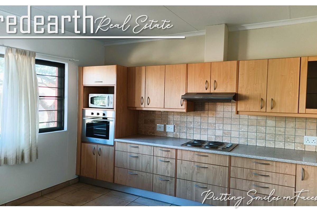 A functional kitchen featuring light wood-finish cabinetry, built-in oven and microwave, electric hob, extractor fan, and tiled splashback with neutral floor tiles.