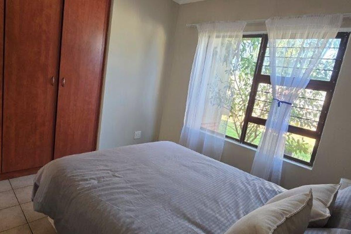 A functional bedroom featuring built-in wooden cupboards, tiled flooring, and a window fitted with security bars.