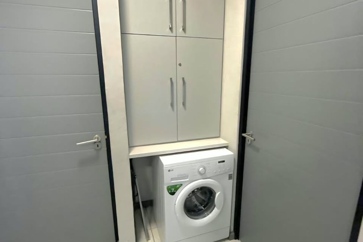 A compact laundry area featuring built-in floor-to-ceiling cabinetry and tiled flooring, positioned between two internal doors.