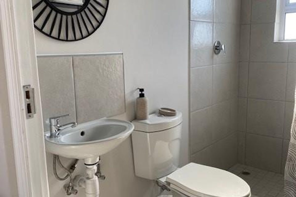 A functional bathroom featuring a wall-mounted basin, close-coupled toilet, and a tiled shower enclosure with neutral finishes.