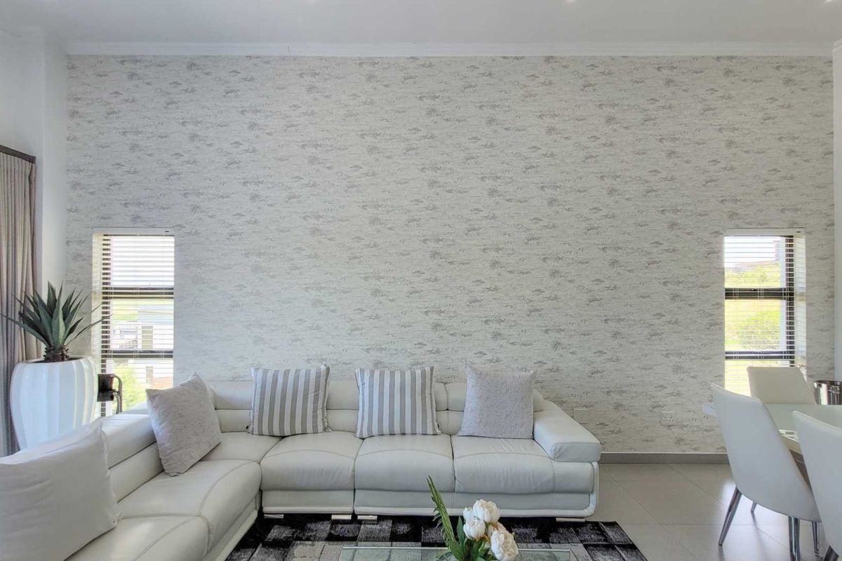 A bright and modern living area featuring a large feature wall with textured wallpaper, flanked by two vertical windows with fitted blinds.