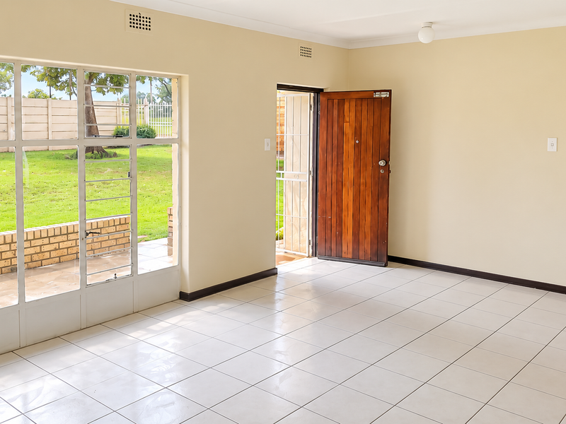 Bright and spacious living area featuring neutral tiled flooring, large windows providing garden views, and direct access to the exterior.
