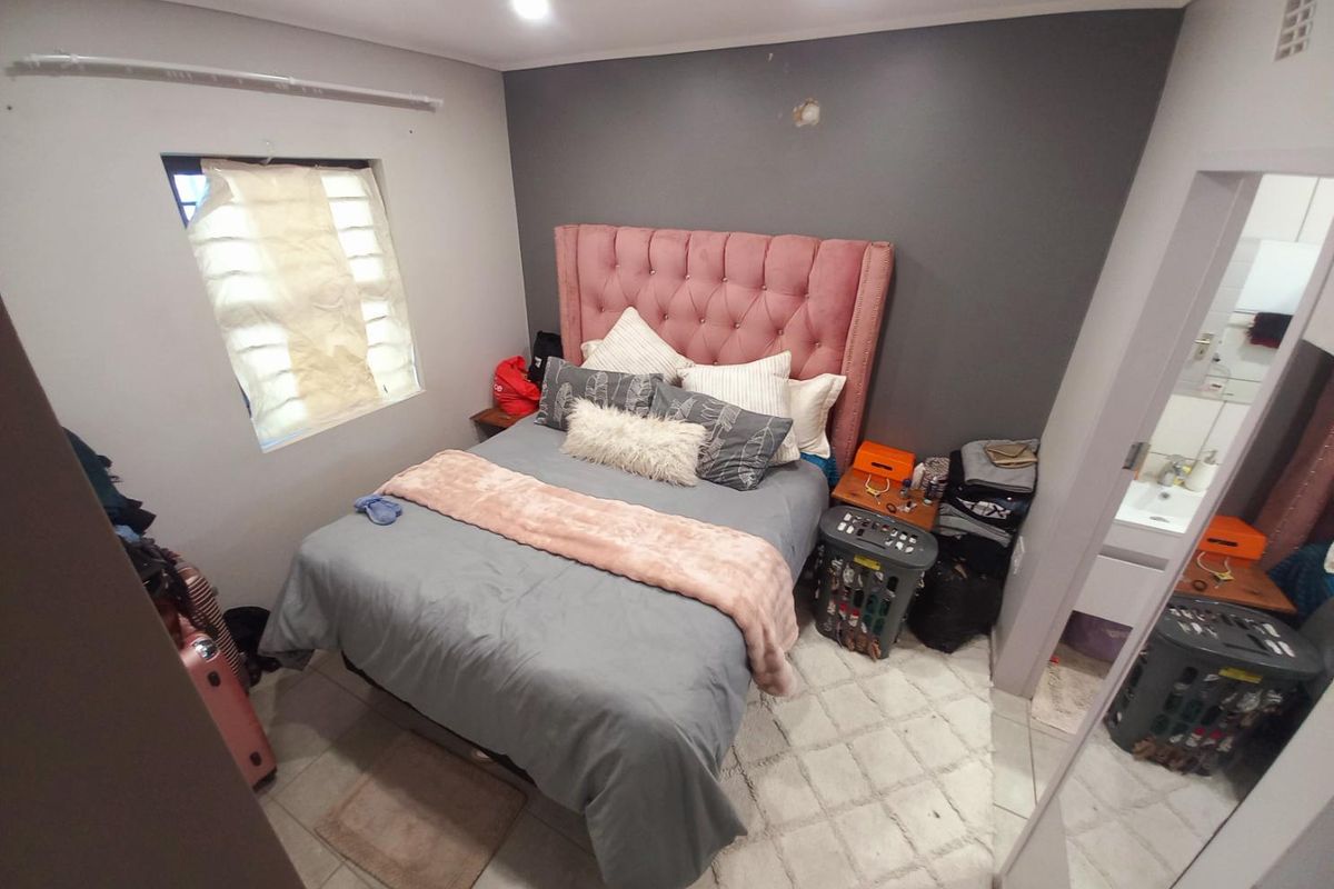 A compact bedroom featuring tiled flooring, a feature wall, and an adjoining en-suite bathroom area.