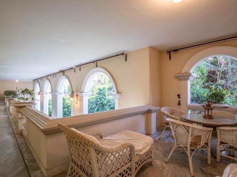 A spacious covered balcony featuring elegant arched windows, marble flooring, and a classic balustrade, offering a bright and airy outdoor living space.