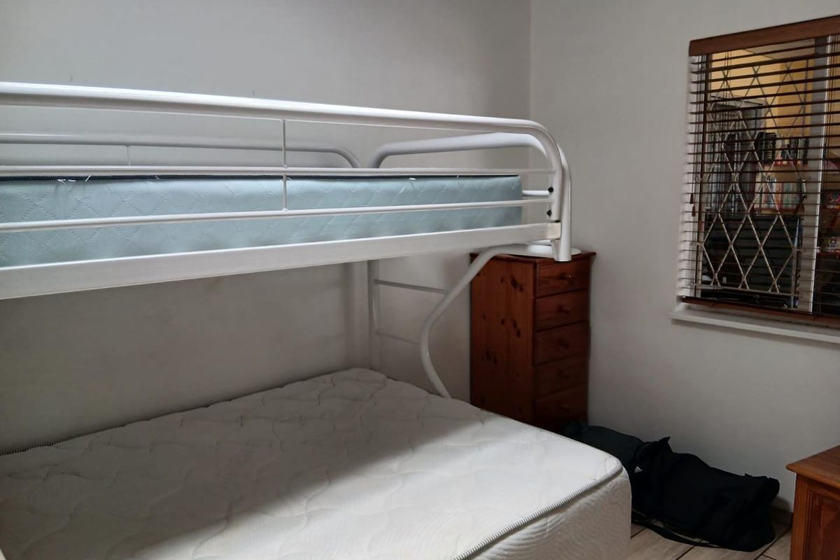 A functional bedroom featuring tiled flooring and a window fitted with wooden blinds.