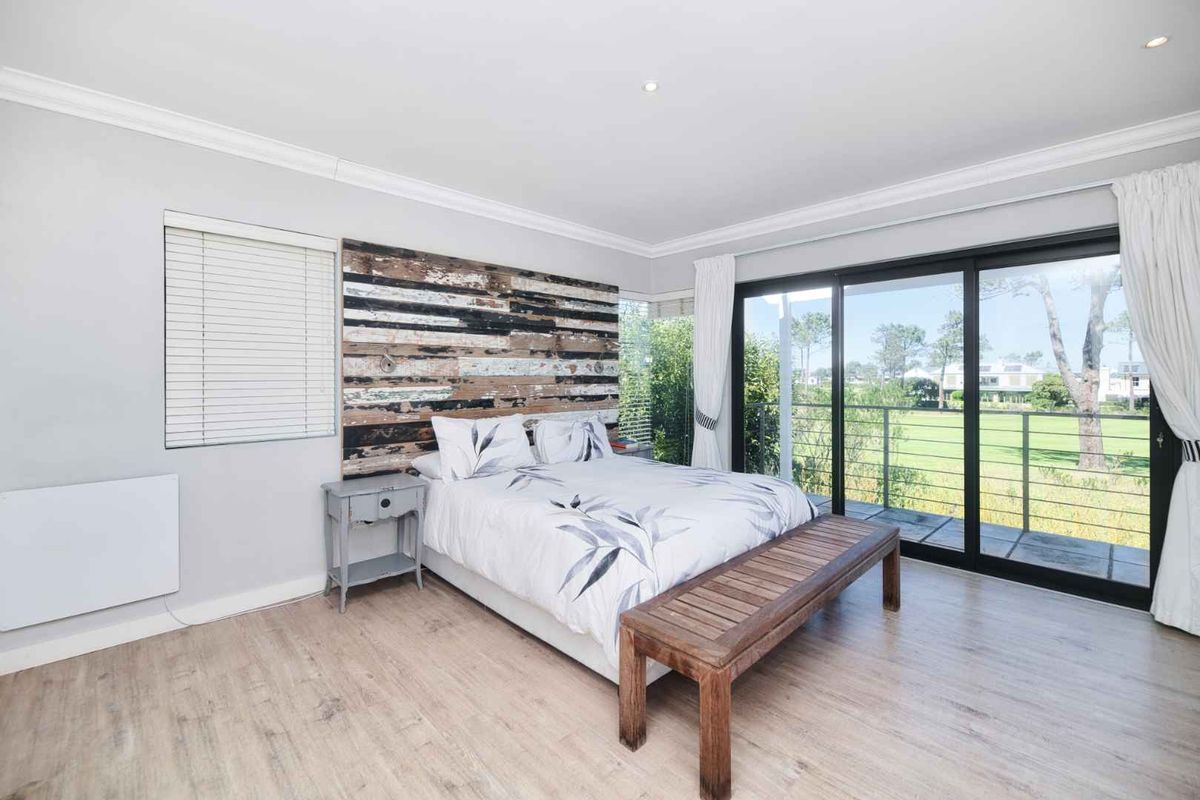 A bright bedroom featuring laminate flooring, recessed lighting, and large sliding glass doors that open onto a balcony with scenic views.