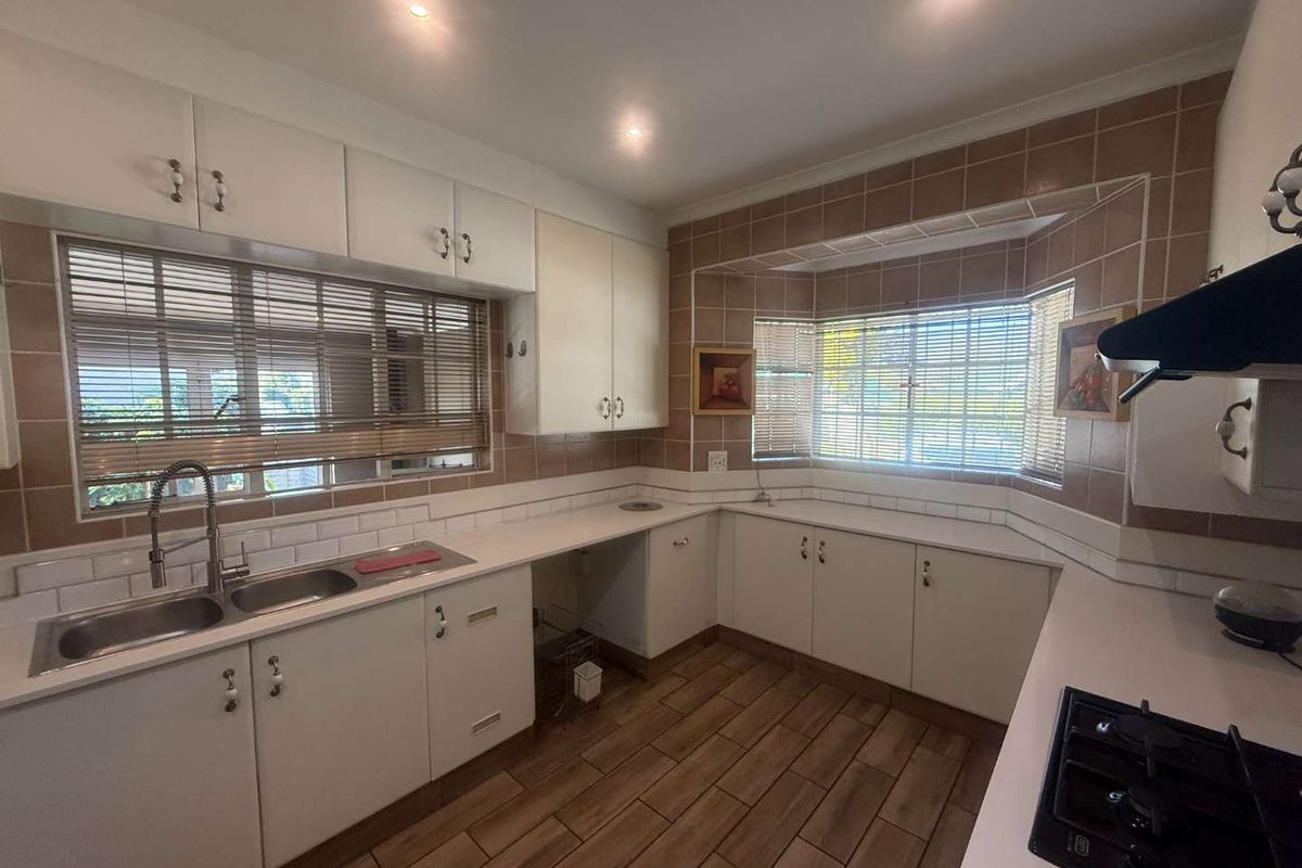 A functional kitchen featuring white cabinetry, a double basin sink, gas hob with extractor, and tiled backsplash with wood-look flooring.