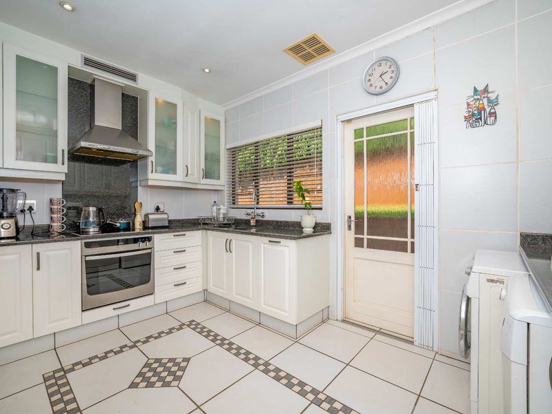 Functional kitchen featuring white cabinetry, granite countertops, stainless steel appliances, and tiled flooring with a direct access door to the exterior.
