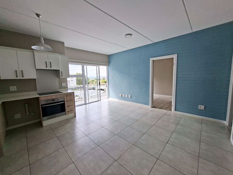 Bright open-plan living area featuring a modern kitchen with built-in appliances, tiled flooring, and a sliding door leading to an outdoor balcony.
