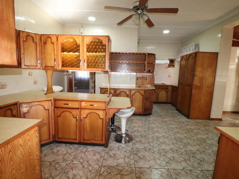 Spacious kitchen featuring extensive wooden cabinetry, tiled flooring, and a breakfast bar area, offering significant potential for a modern renovation.